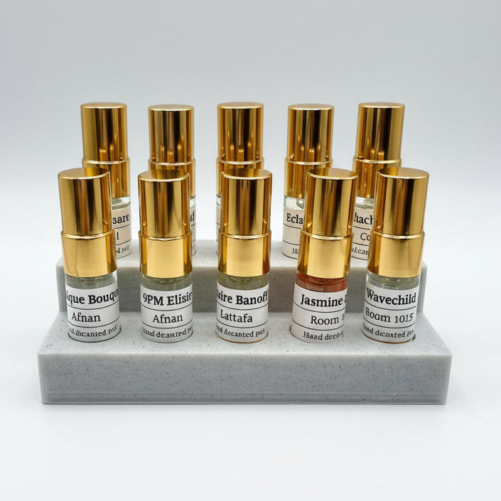 Set of small perfume bottles with gold caps on a gray stand against a white background
